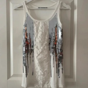 Vit paljettprydd linnetopp - Säljer en vit linnetopp med dekorativa paljetter i silver framtill. Toppen har ett snyggt mönster i mitten.