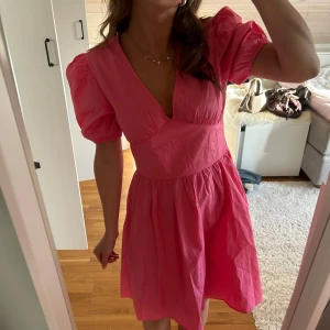 Rosa med puffärmar - Så söt rosa klänning med puffärmar och v-ringning. Klänningen har en markerad midja, kort kjol och öppen rygg. Perfekt till sommaren! 