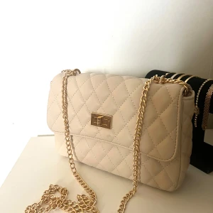 Beige axelväska med guldkedja - Säljer en beige  axelväska med snygg justerbar guldkedja. Väskan är i nyskick och är aldrig använd!