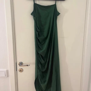 Grön långklänning - Säljer en elegant grön långklänning med smala axelband och snygg drapering framtill. Klänningen har en rak och tight i passform och är tillverkad i ett mjukt, slätt material som faller fint. Perfekt för dig som vill sticka ut med en stilren look.