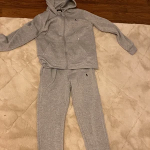 Grå hoodie från Polo Ralph Lauren - Mysig grå hoodie med dragkedja och huva från Polo Ralph Lauren. Klassisk design med liten broderad logga på bröstet och långa ärmar. Perfekt för chill dagar eller när du vill vara bekväm. Och byxkor med den