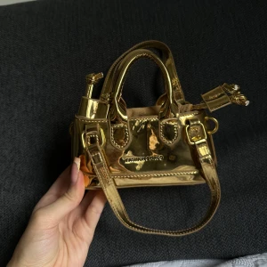 Guldig minihandväska med metallic finish - Säljer en liten och glansig guldig handväska. Väskan har metallic finish å endast blivit använd en gång 