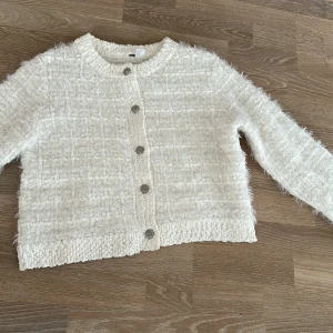 Vit fluffig kofta med silvriga knappar - Superfin vit kofta från H&M i fluffigt material med dekorativa silvriga knappar framtill. Koftan har lång ärm och en lite boxig, croppad passform. Perfekt att slänga på sig för en mysig och stilren look.