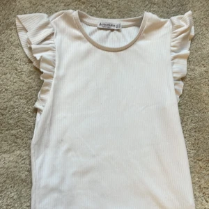 Vit ribbad topp - Säljer en söt vit ribbad topp från Stradivarius med volangdetaljer på axlarna. Perfekt nu till sommaren! ☀️ 
