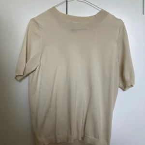 Beige stickad tröja från Lindex - Säljer en enkel och stilren beige stickad tröja från Lindex. Tröjan har korta ärmar och rund halsringning, perfekt för lager-på-lager eller som den är. Passar till många olika outfits!