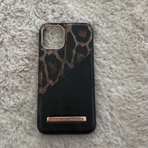 Leopardmönstrat mobilskal från iDeal of Sweden iPhone 12 mini - Snyggt mobilskal med leopardmönster och svart skinnimitation från iDeal of Sweden. Skalets ovandel har ett djurmönster i brunt och svart, medan nederdelen är helsvart med en guldfärgad logga. Perfekt accessoar för att ge mobilen en trendig look. För iPhone 12 mini. Använd fåtal gånger lite sliten på skalet annars bra