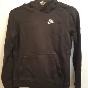 Svart hoodie från Nike - Säljer en svart hoodie från Nike med vit logga på bröstet. Tröjan har huva, magficka och långa ärmar. Perfekt för en sportig och avslappnad stil.