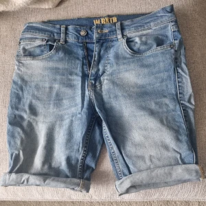 Ljusblå jeansshorts - Säljer ett par ljusblå jeansshorts från WRKRT med klassisk femficksdesign och uppvikta benslut. Shortsen har knapp- och dragkedjestängning samt bälteshällor. Perfekta för varma dagar!