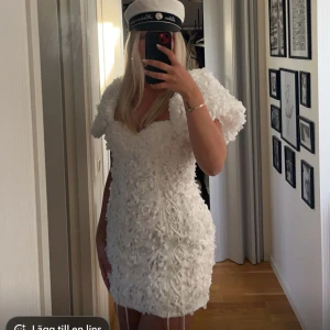 Vit kortklänning med 3D-blommor - Superfin vit kortklänning med puffärmar och 3D-blommor över hela klänningen. Klänningen har en markerad byst och figurnära passform, perfekt för student eller sommarfest. Materialet känns lyxigt och detaljerna gör den unik.