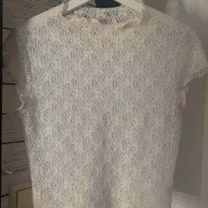 Vit spetsblus med kort ärm - Säljer en söt vit blus i spets med korta ärmar. Toppen har ett feminint mönster och är perfekt för dig som gillar romantisk stil. Den är lätt och luftig, passar bra till både jeans och kjol.