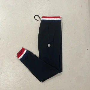 Mockler byxa - Snygga svarta byxor från Moncler med resår i midjan och benslut i rött, vitt och blått. Byxorna har en liten Moncler-logga på benet och är perfekta för en sportig och stilren look.
