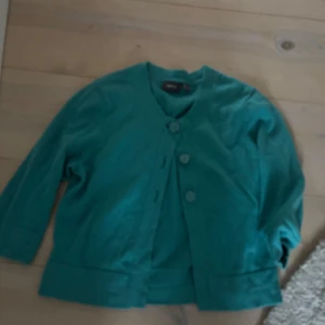 Turkos kavaj med knappar - Snygg turkos kavaj med tre stora knappar framtill och rundad halsringning. Jackan har trekvartsärm och en rak, lite boxig passform. Perfekt för att addera färg till din outfit.