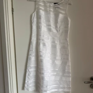 Vit ärmlös klänning från s.Oliver Black Label - Säljer en elegant vit ärmlös klänning från s.Oliver Black Label. Klänningen har diskreta horisontella ränder i tyget och en klassisk, rak passform. Perfekt för somriga tillfällen eller studentfirande.