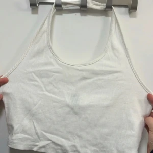 Vit ribbad halterneck linnetopp - Säljer en vit ribbad halterneck linnetopp med croppad passform. Perfekt för varma dagar och enkel att matcha med olika outfits. Tunt och mjukt material som känns skönt mot huden.