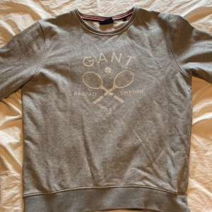 GANT hoodie - Säljer en GANT hoodie utan luva med ett tennis tryck på framsidan. Det är i storlek S och har inte använts på många år, det är PYTTE litet hål på framsidan men man märker inte av det något alls. Jag har ärvt den av min bror men aldrig använts. 