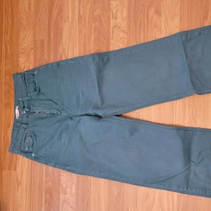 Gröna raka jeans - Säljer ett par gröna jeansbyxor med klassisk femficksdesign och raka ben. Byxorna har normal passform och stängs med dragkedja och knapp. Perfekta för dig som gillar enkel och stilren look.