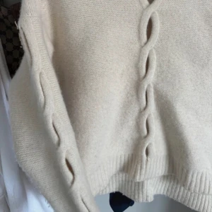 Krämvit stickad kofta från Filippa K - Säljer en krämvit stickad kofta från Filippa K med snygga flätade detaljer längs ärmar och framtill. Koftan har lång ärm och ribbade muddar vid ärmslut och nederkant. 