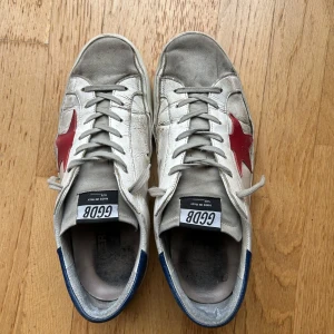 Golden goose skor med röd stjärna - Säljer ett par Golden Goose skor med grå detaljer och en röd stjärna på sidan. Skorna är använda och i hyfsat bra skick och går fortfarande att använda bra. Box ingår. Pris kan diskuteras 