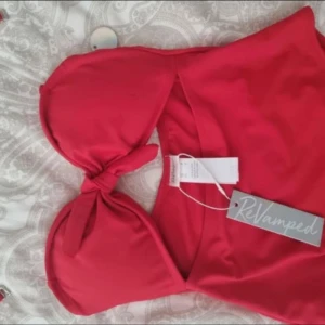 Röd baddräkt från ReVamped - Snygg röd baddräkt från ReVamped med knyt-detalj framtill och avtagbara axelband. Baddräkten har en feminin passform och är tillverkad i ett mjukt material som känns bekvämt mot huden. Perfekt för strand eller pool!