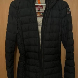 Svart pufferjacka från Parajumpers - Säljer en svart pufferjacka från Parajumpers med huva och dragkedja. Jackan har quiltad design och en insida i ljusare färg samt en praktisk innerficka märkt 'Security Pocket'. Perfekt för kyligare dagar.