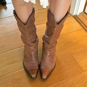 Bruna cowboy boots -  Bruna riktiga cowboy boots från Wrangler med broderade detaljer. Skorna har en stadig klack och är tillverkade i äkta läder. De är bekväma och rymliga framtill. Perfekta till sommaren!!💕lädret på insidan av ena skon har slitits men det är inget som syns på utsidan🫶