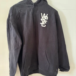 Svart hoodie från WESC - Säljer en svart hoodie från WESC i storlek medium. Tröjan har en vit logga på bröstet, huva med dragsko och en stor magficka. Perfekt för en avslappnad stil och enkel att matcha med det mesta.