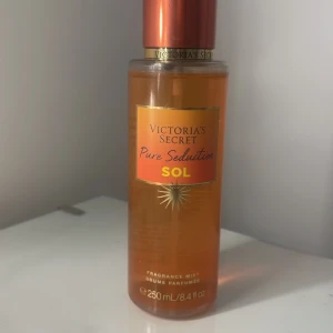 Victoria's Secret Pure Seduction Sol Body Mist - En kroppsspray från Victoria's Secret i doften Pure Seduction Sol. Flaskan är orange med guldiga detaljer och rymmer 250 ml. Doften har inslag av orange mimosa och saftig ananas för en fräsch och somrig känsla.