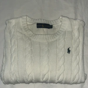 Vit kabelstickad tröja från Ralph Lauren - Säljer en klassisk vit kabelstickad tröja från Ralph Lauren med rund halsringning och broderad logga på bröstet. Tröjan har långa ärmar och ribbade muddar. Perfekt för en stilren och tidlös look. PRIS DISKUTERBART
