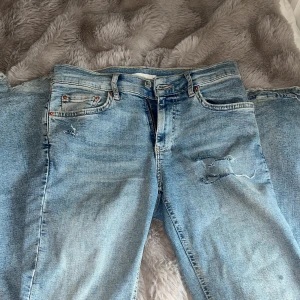 Ljusblå slitna jeans med hål - säljer ett par ljusblå jeans med slitningar och hål på både lår och knä. jeansen har en bootcut passform och är lågmidjade. säljer då de inte används, har några slitningar nertill då de är för långa för mig