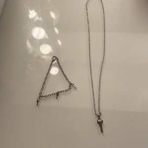 Silverfärgat smyckeset med nyckelberlocker - Säljer ett set med halsband och armband i silverfärgad metall. Halsbandet har en tunn kedja med en liten nyckel som hänge. Armbandet har tre små nyckelberlocker längs en grov kedja. Perfekt för dig som gillar unika detaljer!