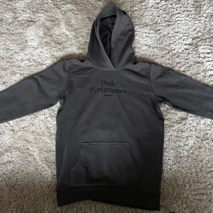 Mörkgrå hoodie från Peak Performance - Säljer en mörkgrå hoodie från Peak Performance med broderad logga på bröstet. Tröjan har huva och en stor magficka framtill. Perfekt för en avslappnad och sportig stil.