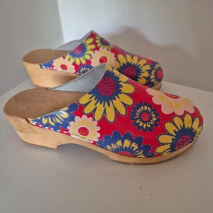 Träskor från Mohedatoffeln - Färgglada trätofflor från Mohedatoffeln med stort blommönster i rött, gult och blått. Använda ett fåtal gånger. Strl 38. 