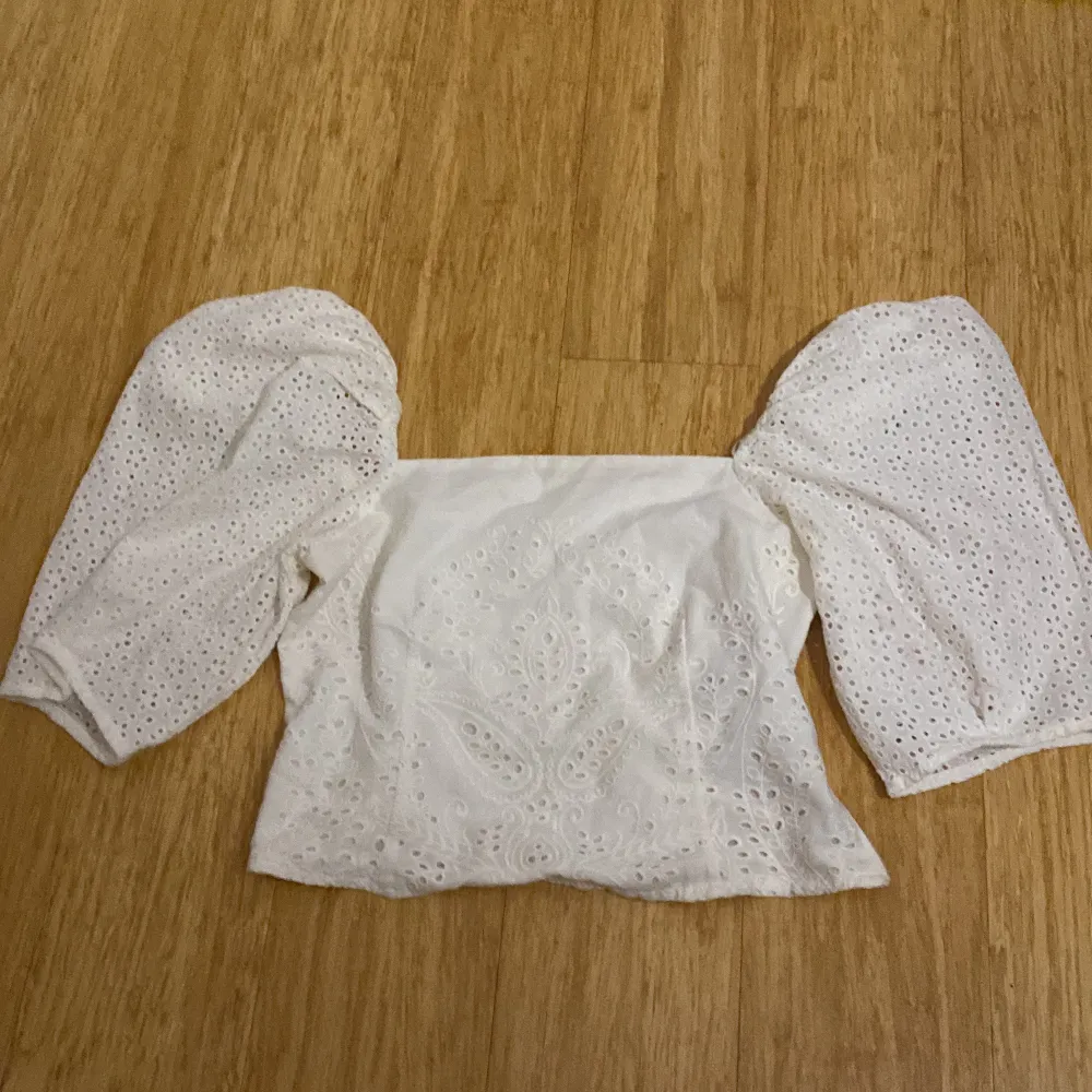 Superfin vit blus från H&M med broderade detaljer och stora puffärmar. Blusen är axelbandslös och har ett romantiskt hålmönster i tyget. Perfekt för vår och sommar!. Yläosat.