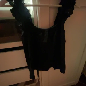 Svart linnetopp med volang från JDY - Säljer en svart linnetopp från JDY med breda axelband dekorerade med volang.