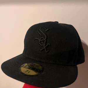 Svart keps New Era Chicago White Sox - Säljer en svart keps från New Era med Chicago White Sox-logga broderad framtill. Klassisk 59FIFTY-modell med platt skärm och broderade detaljer. Perfekt för dig som gillar sportiga accessoarer.