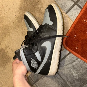 Nike Air Jordan 1 Retro High Shadow - Säljer ett par Nike Air Jordan 1 Retro High Shadow med svart och grå färgkombination. Skorna har klassisk snörning, rund tå och platt sula. Perfekta för dig som gillar streetwear och vill ha en ikonisk sneaker i garderoben.