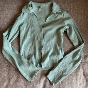 Ljusgrön ribbad kofta med knappar - Det Säljer en ljusgrön kofta med ribbad struktur och långa ärmar. Tröjan har v-ringning, klassisk krage och knäppning framtill. 