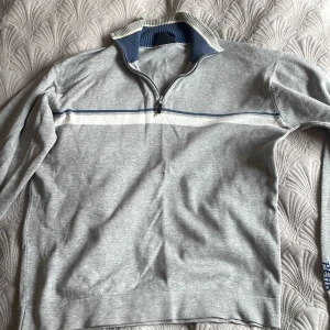 Grå halvzip tröja från Peak Performance - Säljer en grå långärmad tröja från Peak Performance i storlek M. Tröjan har halv dragkedja, vit och blå rand över bröstet samt broderad Peak-logga vid nederkanten. Perfekt för lager-på-lager och snygg till jeans. Tröjan är i äldre modell men sparsamt använd och inga tecken på användning.
