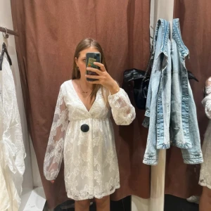Vit blommig klänning med v-ringning från Gina Tricot - Superfin vit klänning från Gina Tricot med v-ringning och långa transparenta ärmar. Klänningen har blommigt mönster i spets och en kort längd. Kläningen är använd en gång i tre timmar på en skolavslutning så den är i nyskick. 