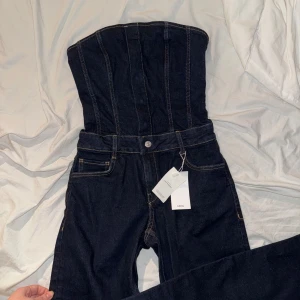 Mörkblå jumpsuit från Mango - Säljer denna virala mörkblåa jumpsuit från Mango i jeansmaterial. Den har en tubtopp-design med markerade sömmar och vida ben. Perfekt för en stilren look. Helt slutsåld, nypris 749kr 