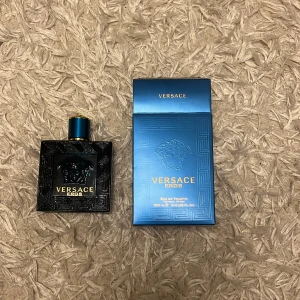 Versace Eros Eau de Toilette 100 ml - Säljer en flaska Versace Eros Eau de Toilette, 100 ml. Flaskan har en elegant design med ett svart mönster och blå detaljer. Förpackningen är i en stilren blå färg med Versace-loggan i guld. Perfekt för den som vill ha en fräsch och maskulin doft. Är sprutad typ 10 gånger.