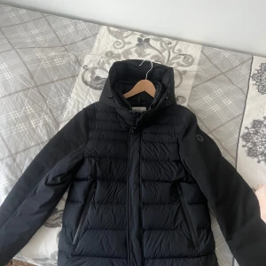 jacka från Moncler - Säljer en stilren svart jacka från Moncler. Jackan har en quiltad design med dragkedja och en praktisk huva. Perfekt för kyliga dagar och håller dig varm och bekväm. En klassisk och tidlös modell som passar till det mesta.