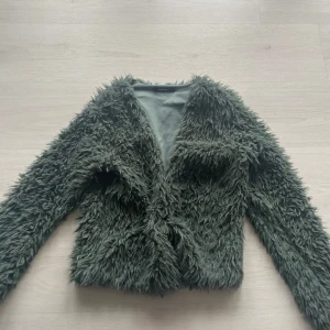 Grön pälsjacka från Gina Tricot - Varm pälsjacka från Gina!! Säljer då den var lite för liten och inte användt jackan på länge. Den är varmare än man tror och brukar ha en klämma för o hålla ihop den