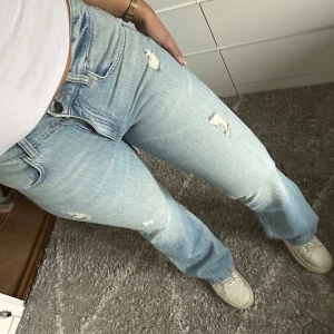 Ljusblå jeans med slitningar - Snygga ljusblå jeans med slitningar och bootcut-stil. De har en klassisk femficksdesign och är perfekta för en avslappnad look. Jeansen har en knapp och dragkedja framtill. Midwaist