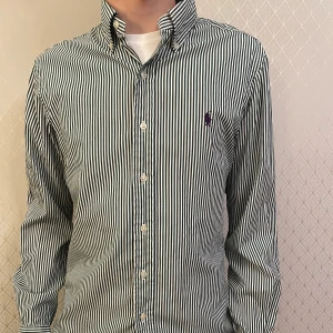 Polo Ralph Lauren skjorta - Snygg randig skjorta från Ralph Lauren i slim fit. Skjortan är grön och vit med långa ärmar och knappar framtill. Perfekt för en stilren look. Nypris på denna är 1999. 