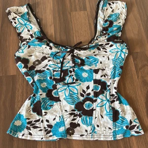 Blommig topp från Jane Norman - Säljer en snygg blommig topp från Jane Norman med turkosa och bruna blommor på en vit bakgrund. Toppen har en v-ringad design. Väldigt 2000-talet stil! 💕