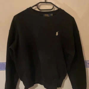 Svart tröja från Polo Ralph Lauren - Säljer en klassisk svart tröja från Polo Ralph Lauren med det ikoniska logotypbroderiet på bröstet. Tröjan har långa ärmar och en rund halsringning. Perfekt för en stilren och avslappnad look.