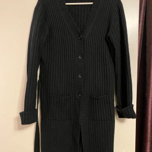 Svart kofta - Svart, ribbstickad kofta med v-ringning, knäppning framtill och två fickor. Koftan har ett avtagbart band i midjan. Jag pendlar mellan s/m och den passar både small och medium. 