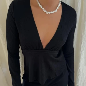Svart omlottopp med knytband - Snygg svart omlottopp med djup v-ringning och långa ärmar. Säljer då den aldrig kommit till användning, slut på hemsidan.