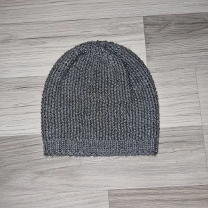 Grå stickad mössa - Säljer en stilren grå stickad mössa. Perfekt för kyliga dagar med sin ribbade design som ger extra värme och komfort. Hemmastickad och är ett måste för höst- och vintersäsongen.